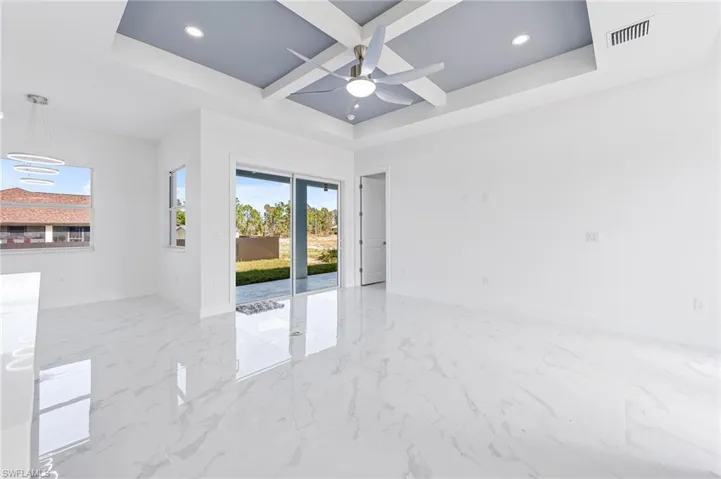 Spare room featuring ceiling fan, beam ceiling, coffered ceiling, a raised ceiling, and light tile patterned floors