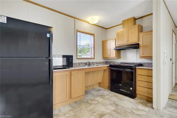 Kitchen with black appliances, ornamental molding, light brown cabinets, and under cabinet range hood
