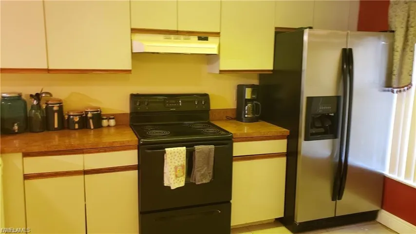 Kitchen featuring black / electric stove, stainless steel fridge, light countertops, and light tile patterned floors