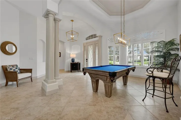 Game room with decorative columns, a raised ceiling, a notable chandelier, light tile patterned flooring, and ornamental molding