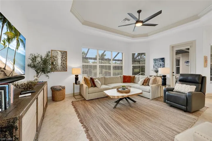 Living room with ceiling fan, crown molding, light tile patterned flooring, and a tray ceiling