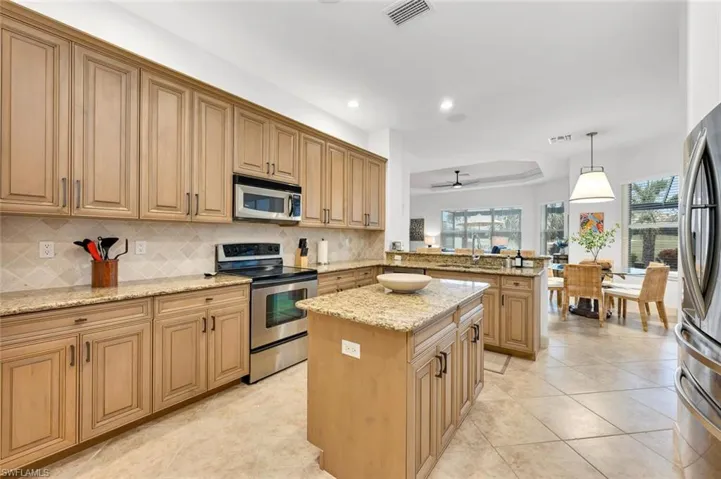 Kitchen with kitchen peninsula, stainless steel appliances, hanging light fixtures, light stone countertops, and a center island