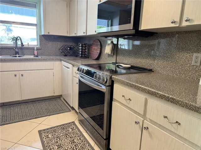 Kitchen with light brown cabinets, backsplash, appliances with stainless steel finishes, light tile patterned floors, and sink