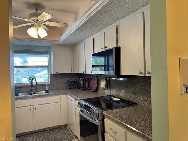 Kitchen with decorative backsplash, a tray ceiling, sink, appliances with stainless steel finishes, and ceiling fan