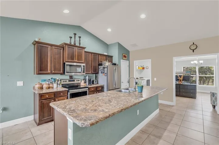 Kitchen with a sink, light tile patterned flooring, lofted ceiling, an island with sink, and appliances with stainless steel finishes