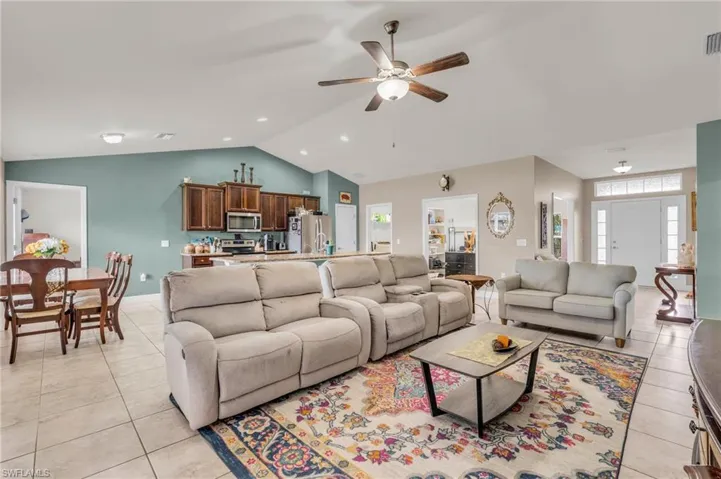 Living room featuring light tile patterned flooring, lofted ceiling, visible vents, and a ceiling fan