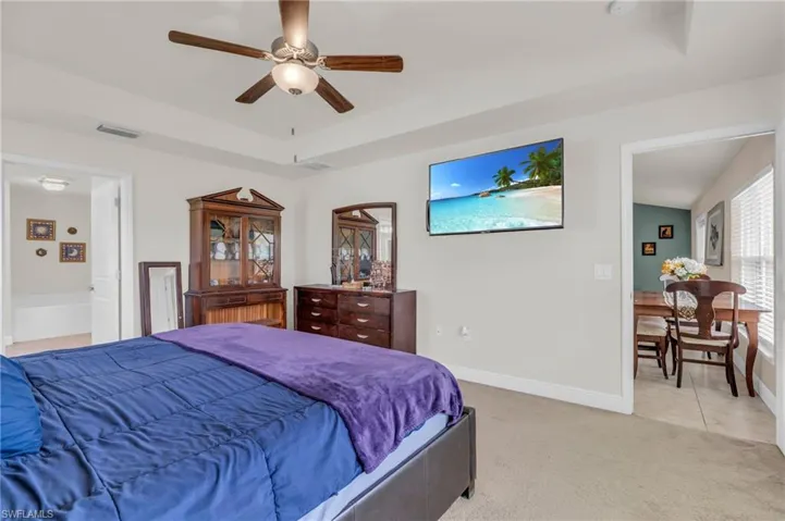 Bedroom featuring a tray ceiling, visible vents, a ceiling fan, baseboards, and light colored carpet