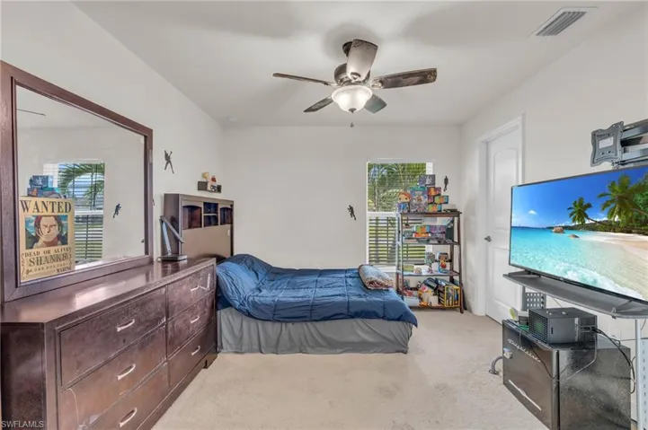 Carpeted bedroom featuring ceiling fan, visible vents, and multiple windows