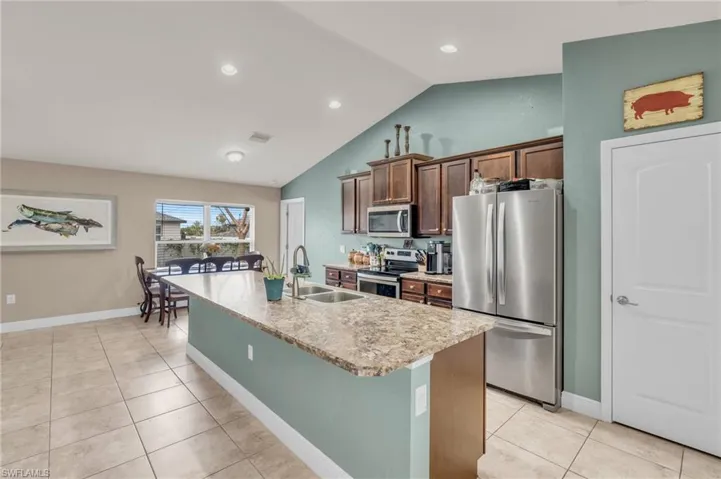 Kitchen with a sink, lofted ceiling, appliances with stainless steel finishes, an island with sink, and light tile patterned floors