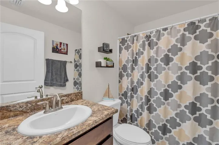 Bathroom featuring toilet, a shower with curtain, vanity, and visible vents