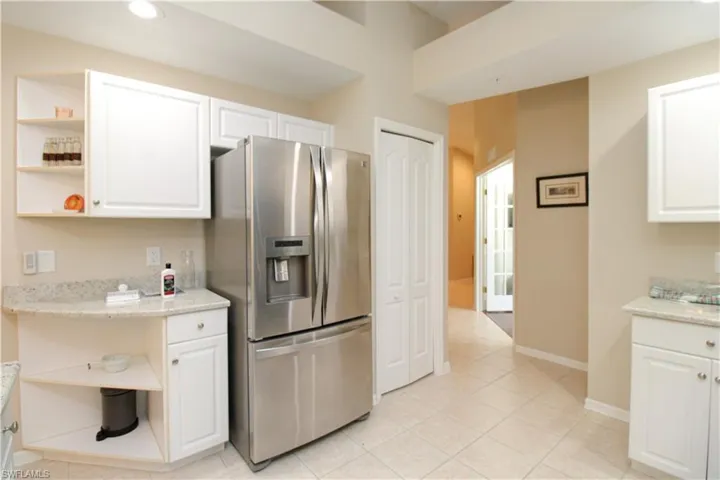 Kitchen with stainless steel fridge, light stone countertops, white cabinetry, and light tile patterned floors