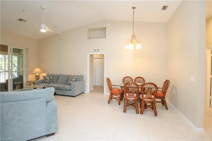 Dining room with light tile patterned floors, ceiling fan with notable chandelier, and lofted ceiling