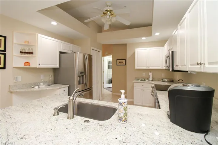 Kitchen featuring light stone counters, stainless steel appliances, ceiling fan, sink, and white cabinetry