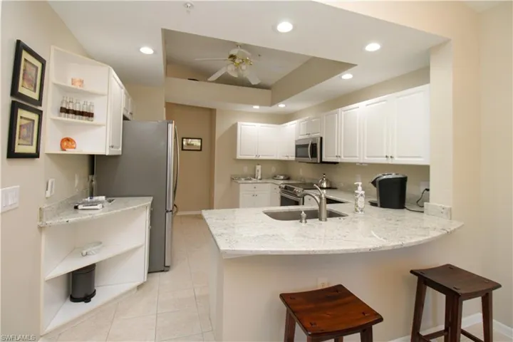 Kitchen with white cabinetry, kitchen peninsula, light stone countertops, and appliances with stainless steel finishes