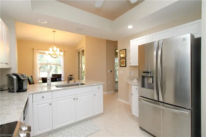 Kitchen with light stone countertops, sink, stainless steel fridge with ice dispenser, a notable chandelier, and white cabinets