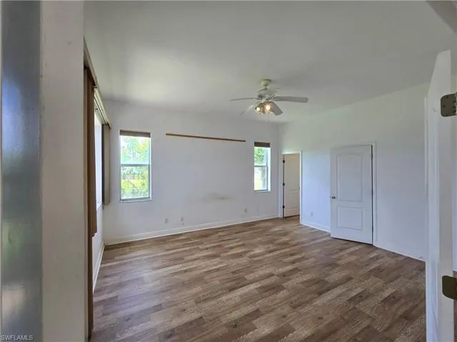Spacious room with wood-finish flooring, multiple windows, a ceiling fan with integrated lighting, and white paneled doors
