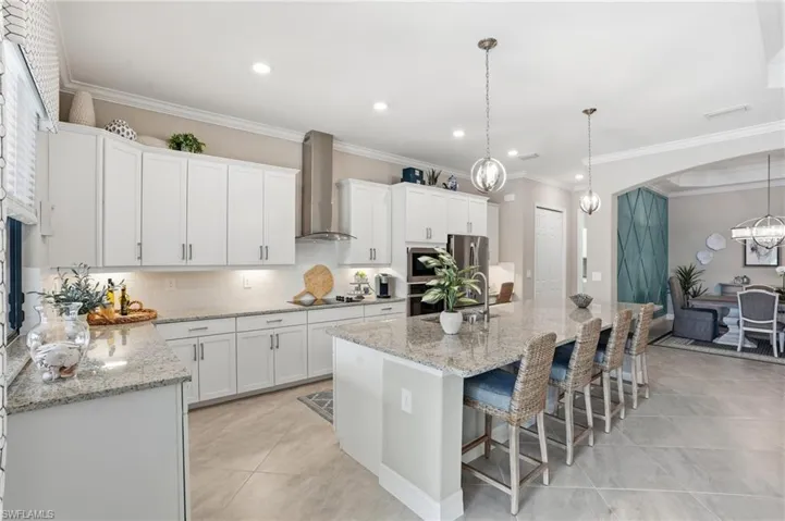 Kitchen featuring crown molding, backsplash, a breakfast bar, light stone countertops, and white cabinets