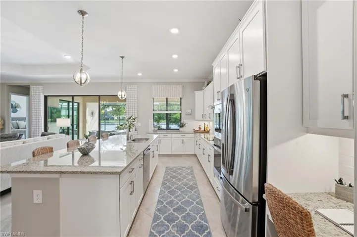 Kitchen with white cabinets, light stone counters, stainless steel appliances, decorative light fixtures, and open floor plan