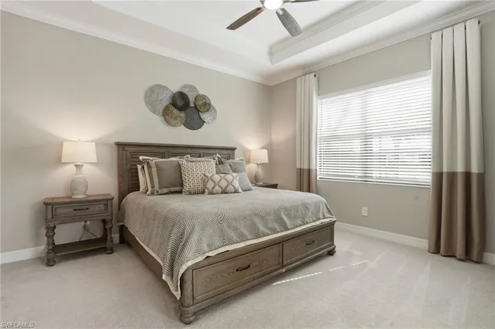 Bedroom featuring a tray ceiling, light carpet, ornamental molding, and ceiling fan