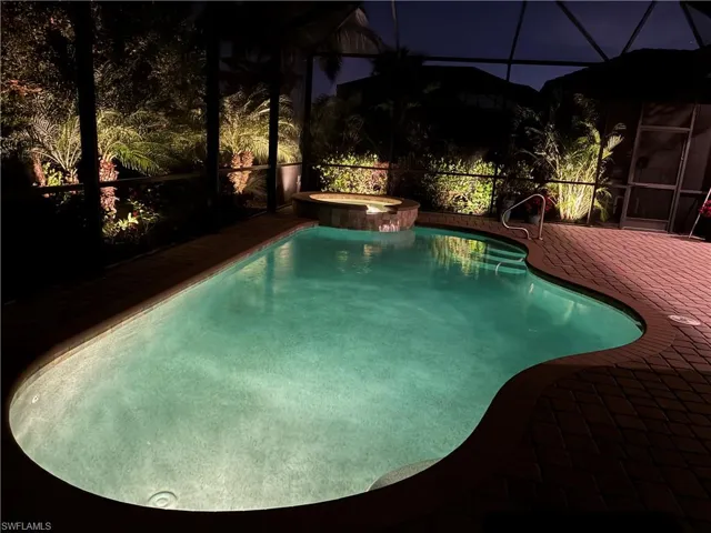 Pool at twilight featuring a lanai, a sunroom, a pool with connected hot tub, and a patio area