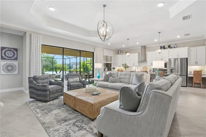 Living room featuring ornamental molding, a tray ceiling, recessed lighting, a chandelier, and light tile patterned flooring