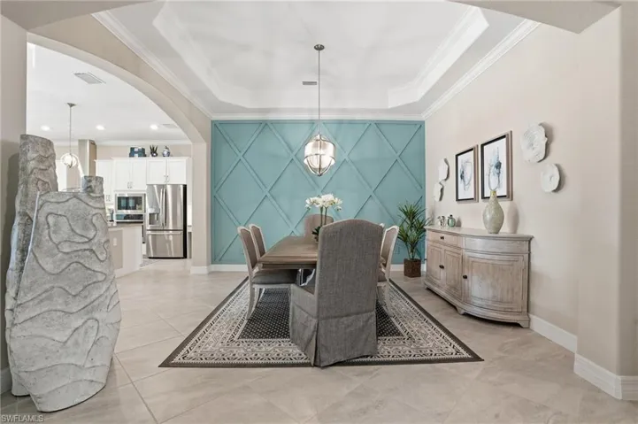 Dining space featuring crown molding, a tray ceiling, arched walkways, and light tile patterned flooring