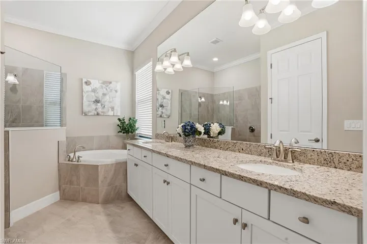 Bathroom featuring a walk in shower, double vanity, crown molding, a garden tub, and light tile patterned floors