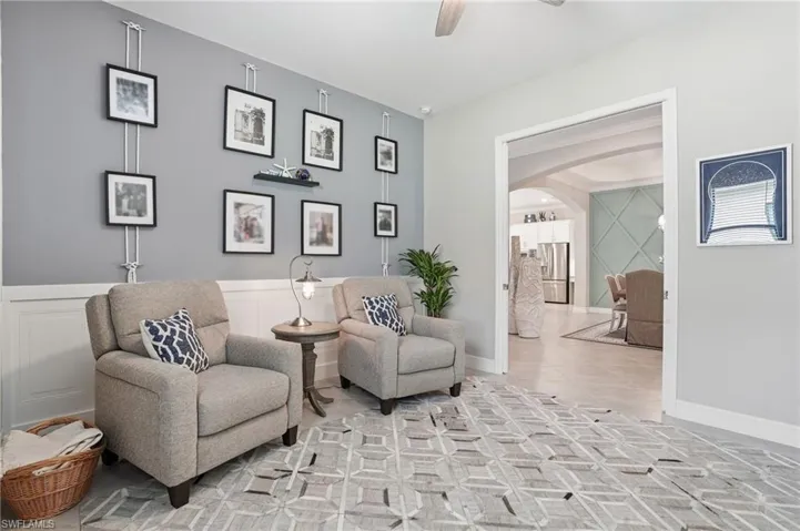 Living area with arched walkways, a ceiling fan, a decorative wall, tile patterned flooring, and a wainscoted wall