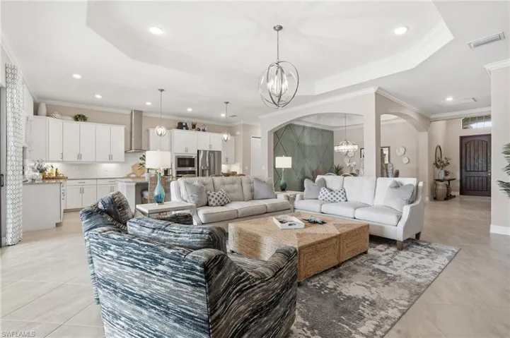 Living room with a raised ceiling, crown molding, a chandelier, recessed lighting, and arched walkways