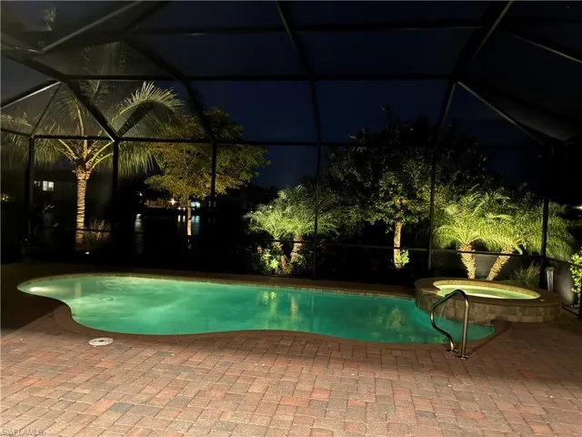 Pool at night featuring a lanai, a sunroom, and a pool with connected hot tub