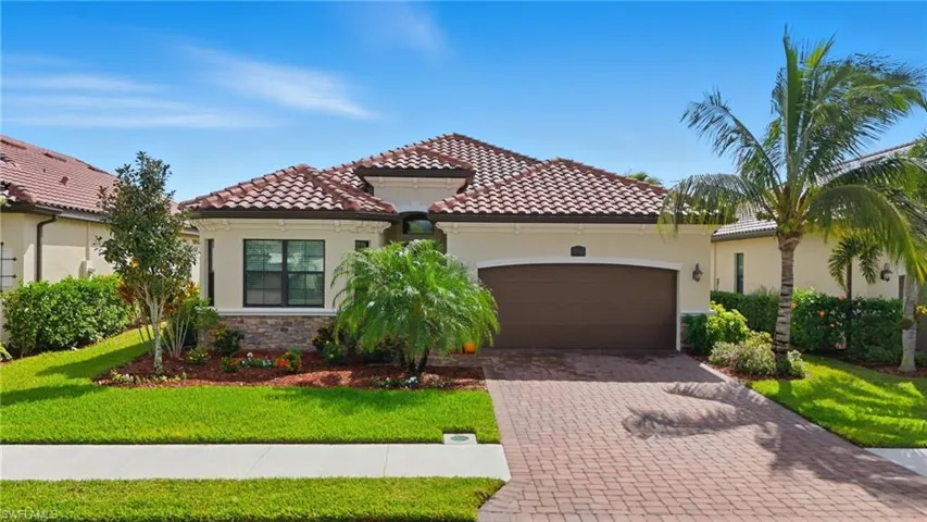 Mediterranean / spanish house with stucco siding, stone siding, an attached garage, decorative driveway, and a front lawn