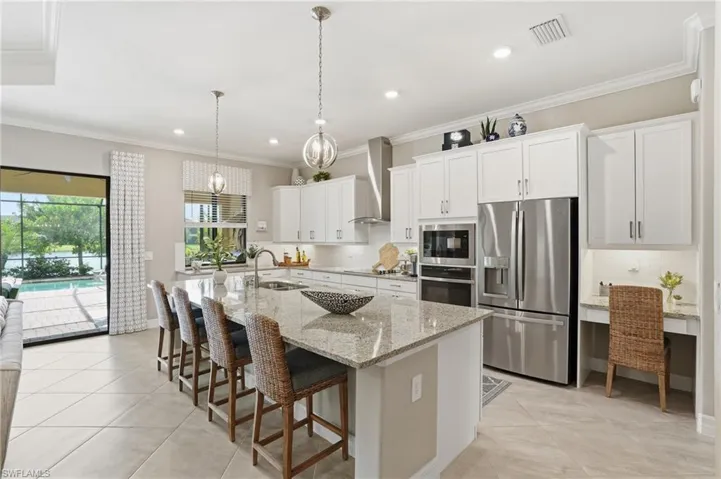 Kitchen featuring ornamental molding, decorative backsplash, appliances with stainless steel finishes, white cabinets, and a kitchen breakfast bar