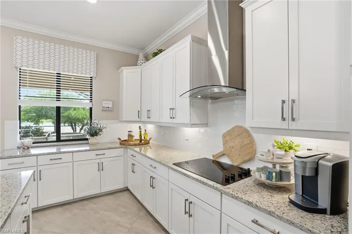 Kitchen featuring crown molding, white cabinetry, wall chimney range hood, tasteful backsplash, and light stone counters
