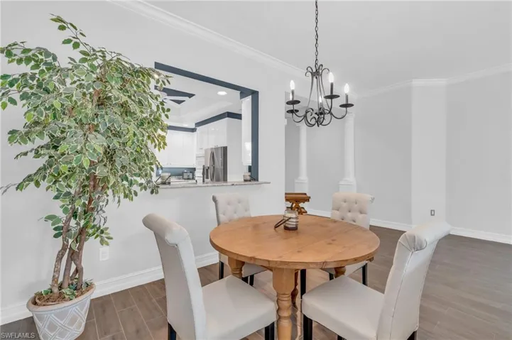 Dining room with ornamental molding, dark hardwood / wood-style floors, decorative columns, and a notable chandelier