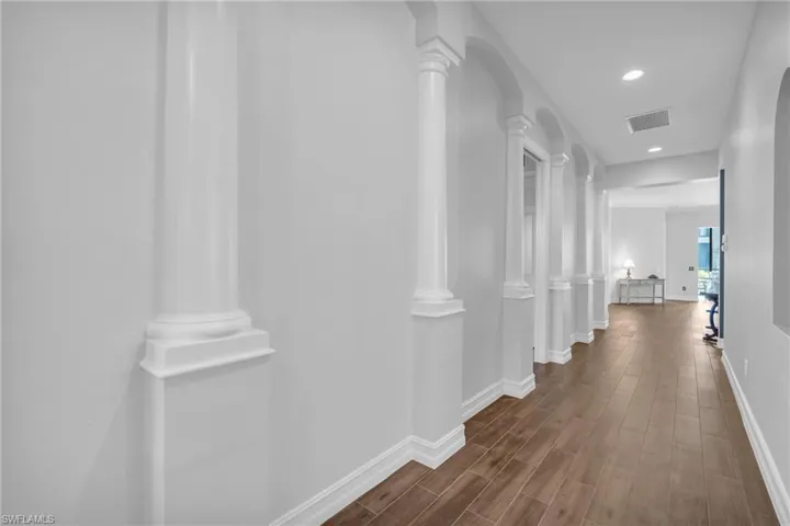 Hallway with decorative columns and wood-type flooring