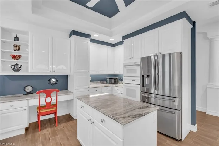 Kitchen with stainless steel refrigerator with ice dispenser, white cabinetry, light stone counters, a center island, and built in desk