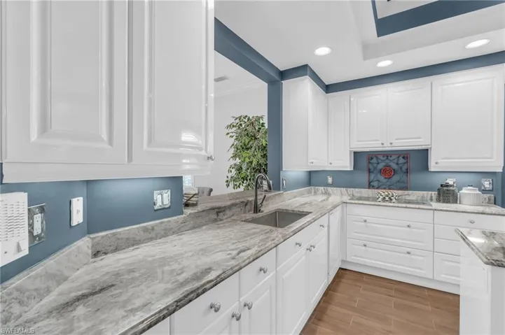 Kitchen with white cabinetry, sink, light stone counters, and black electric cooktop