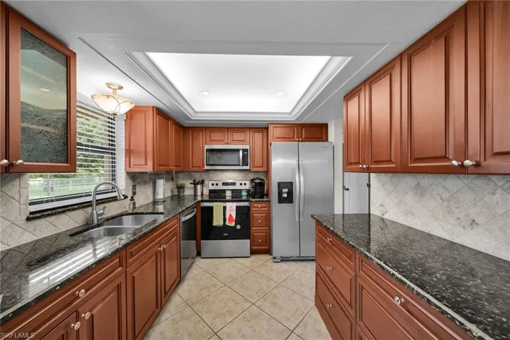 Kitchen with a raised ceiling, sink, backsplash, appliances with stainless steel finishes, and dark stone countertops