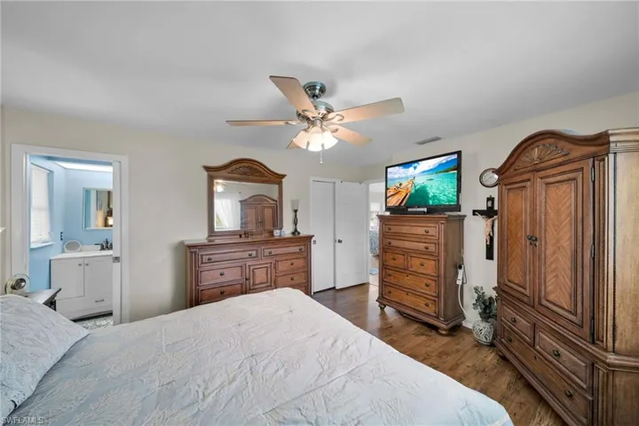 Bedroom with connected bathroom, multiple windows, ceiling fan, and dark hardwood / wood-style floors