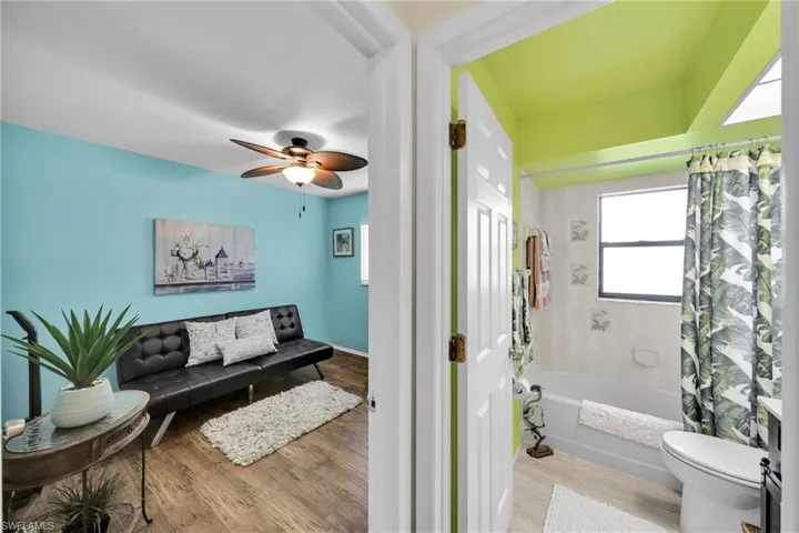 Bathroom with ceiling fan, hardwood / wood-style floors, toilet, and shower / bathtub combination with curtain
