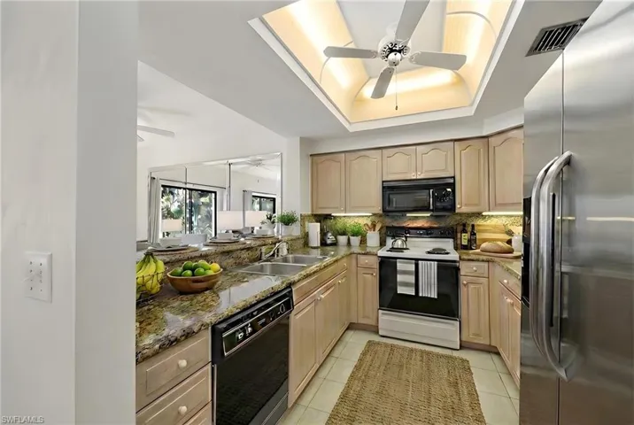 Kitchen with black appliances, dark stone countertops, light wood finish cabinets, a tray ceiling, and tasteful backsplash
