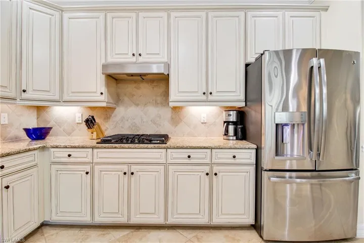 Kitchen featuring stainless steel fridge, black gas stovetop, under cabinet range hood, backsplash, and light stone countertops