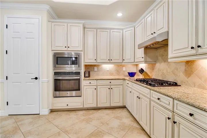 Kitchen featuring decorative backsplash, appliances with stainless steel finishes, under cabinet range hood, and crown molding