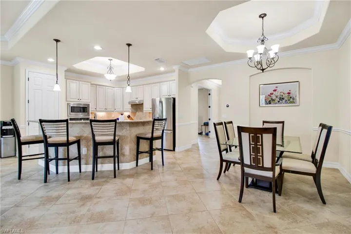 Dining room with a tray ceiling, crown molding, visible vents, arched walkways, and an inviting chandelier