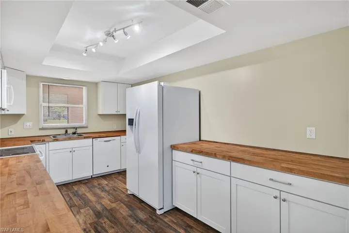 Kitchen with butcher block counters, white cabinetry, white appliances, a raised ceiling, and dark wood-type flooring