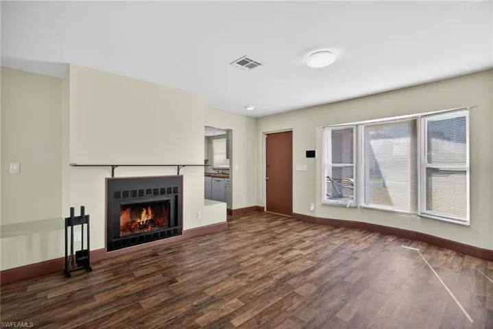 Unfurnished living room with a lit fireplace and dark wood-style floors