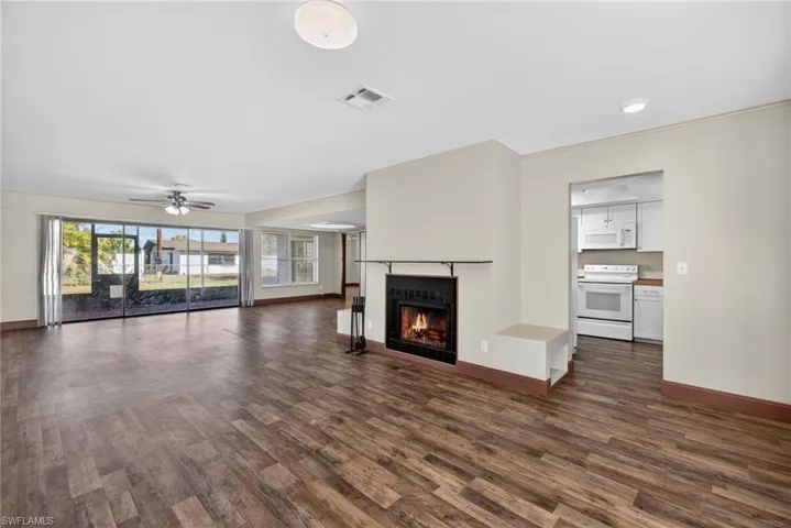 Unfurnished living room with a warm lit fireplace, a ceiling fan, and dark wood-style flooring
