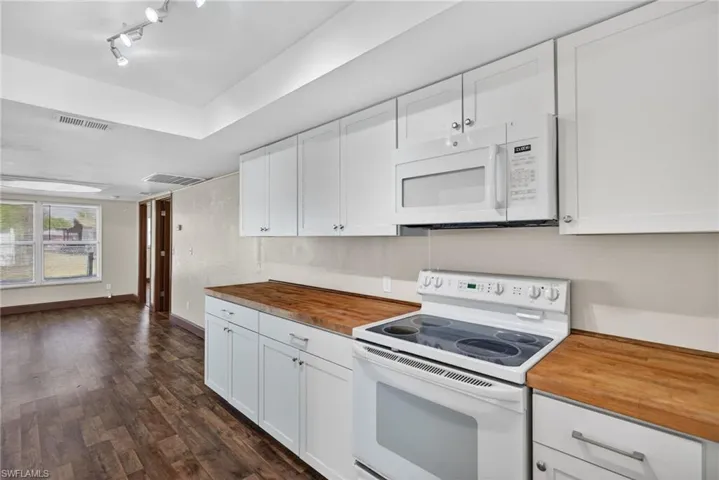 Kitchen featuring white appliances, white cabinetry, wood counters, and dark wood-style floors