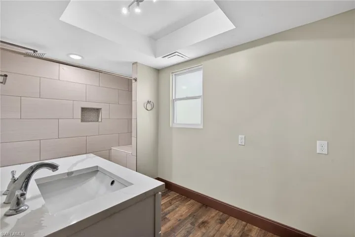 Bathroom with vanity, a tray ceiling, a shower, and dark wood finished floors