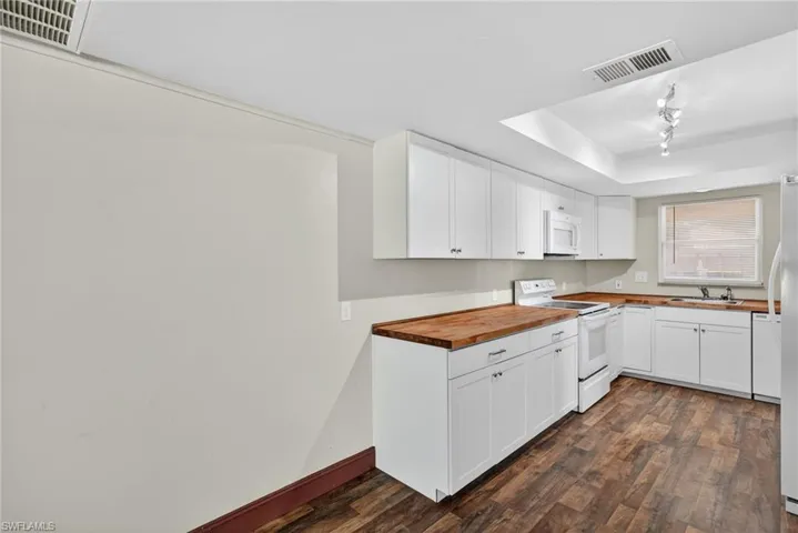 Kitchen with butcher block counters, white appliances, white cabinets, and a tray ceiling